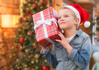 Image showing Boy Wearing Santa Hat Holding Christmas Gift In Front of Tree