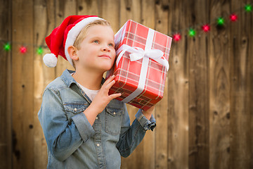 Image showing Curious Boy Wearing Santa Hat Holding Christmas Gift On Wood