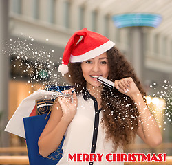 Image showing Christmas shopping, girl holding colorful shopping bags wearing santa hat 