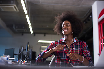 Image showing black woman in modern office speeking on phone over earphones