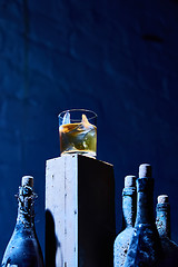 Image showing Glass of whiskey with ice on old wooden bar around the  bottles