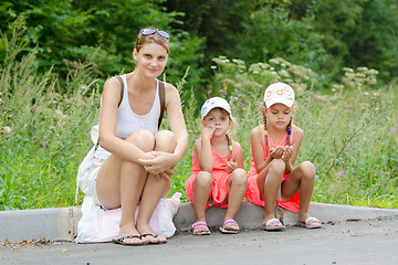 Image showing Mother and two children sitting on the curb of the road waiting for the bus