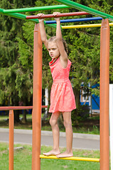 Image showing The girl in the pink dress on the horizontal bar climbing on playground