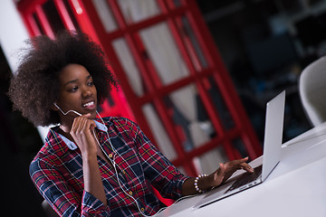 Image showing black woman in modern office speeking on phone over earphones