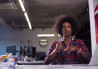 Image showing black woman in modern office speeking on phone over earphones