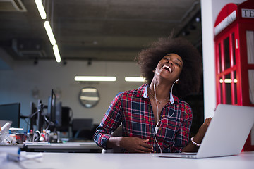 Image showing black woman in modern office speeking on phone over earphones