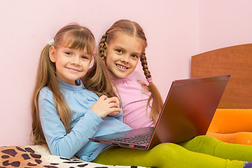 Image showing Two girls sitting on a bed with a laptop and a fun look into the frame