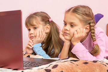 Image showing Two girls lying on his stomach on the bed looking at the laptop screen