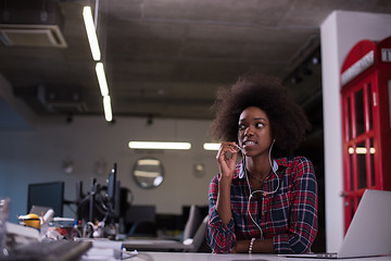 Image showing black woman in modern office speeking on phone over earphones