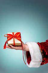 Image showing Hand of Santa Claus holding a gift on blue background