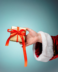 Image showing Hand of Santa Claus holding a gift on blue background