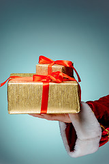 Image showing Hand of Santa Claus holding a gift on blue background