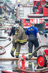 Image showing fire fighter and rescuer walking away building in the drops of water after putting out the