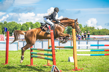 Image showing young, female jockey on her horse leaping over a hurdle.