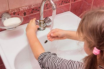 Image showing Five-year girl adjusts the desired flow and temperature of the water flowing from the faucet into the sink