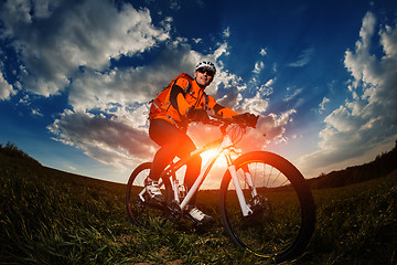 Image showing biker in orange jersey riding on green summer field