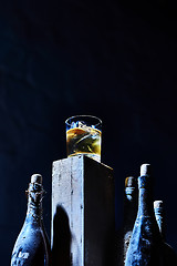 Image showing Glass of whiskey with ice on old wooden bar around the  bottles