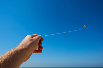 Image showing Male hand holding strings with a kite in sky