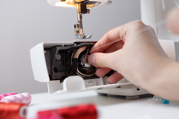 Image showing Hand inserts bobbin in sewing-machine