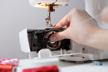 Image showing Arm inserts bobbin in sewing-machine