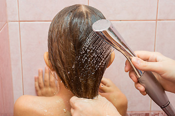 Image showing My mother pours water from a watering can shower on the child\'s hair, close-up