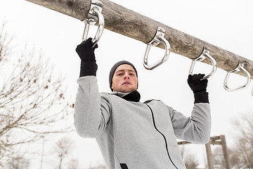 Image showing young man exercising on horizontal bar in winter