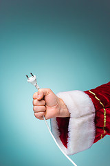 Image showing Hand of Santa Claus holding a electrical plug on blue background