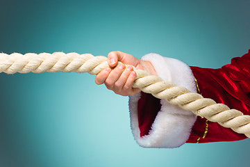 Image showing Hand of Santa Claus pulling the rope on blue background