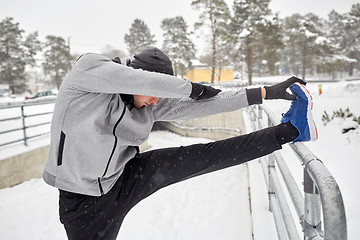 Image showing sports man stretching leg at fence in winter