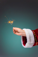 Image showing Hand of Santa Claus holding a sparklers on blue background