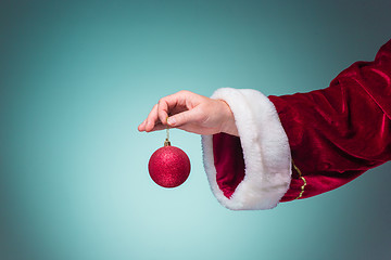 Image showing Hand of Santa Claus holding a Christmas ball on blue background