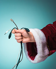 Image showing Hand of Santa Claus holding a bunch connectors to gadgets on blue background