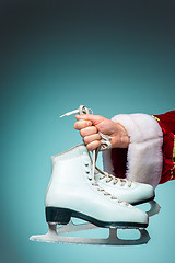 Image showing Hand of Santa Claus holding a figure skates on blue background