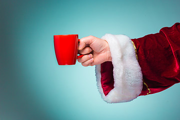 Image showing Hand of Santa Claus holding a red cup on blue background