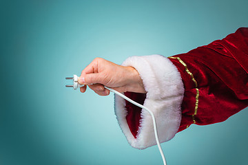 Image showing Hand of Santa Claus holding a electrical plug on blue background