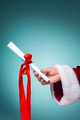 Image showing Hand of Santa Claus holding a gift on blue background