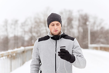 Image showing happy man with earphones and smartphone in winter