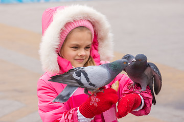 Image showing girl in a pink jacket watching the pigeons that sit on her hands