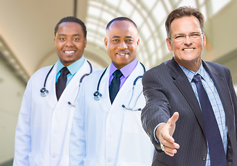 Image showing Mixed Race Doctors Behind Businessman Reaching for Hand Shake In