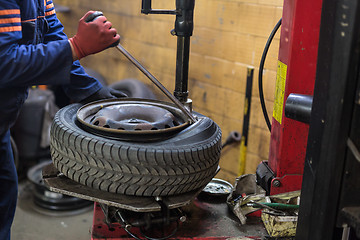 Image showing Professional auto mechanic replacing tire on wheel in car repair service.