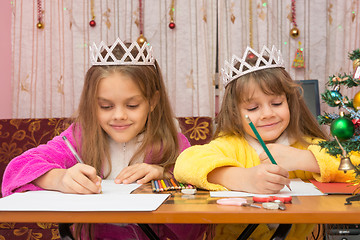 Image showing Two girls happily writing a letter to Santa Claus sitting at a desk in the home environment