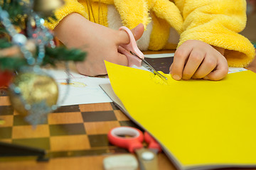 Image showing The child cuts out a star from construction paper, preparing a Christmas crafts, close-up