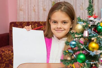 Image showing Happy girl shows a sheet of paper at a table in a Christmas setting