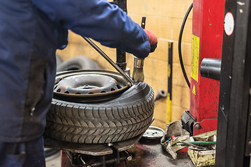 Image showing Professional auto mechanic replacing tire on wheel in car repair service.