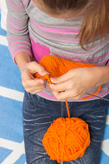 Image showing Top view of the child who knits with needles scarf orange thread