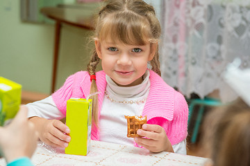 Image showing The girl is drinking juice and eating cookies at the desk in the kindergarten