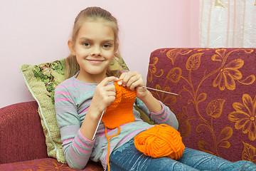 Image showing Girl sitting on the couch, knits on the needles, and looked into the frame