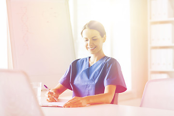 Image showing happy female doctor or nurse writing to clipboard