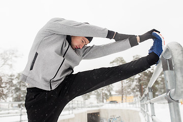 Image showing sports man stretching leg at fence in winter