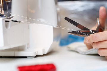 Image showing Seamstress shortens thread with scissors